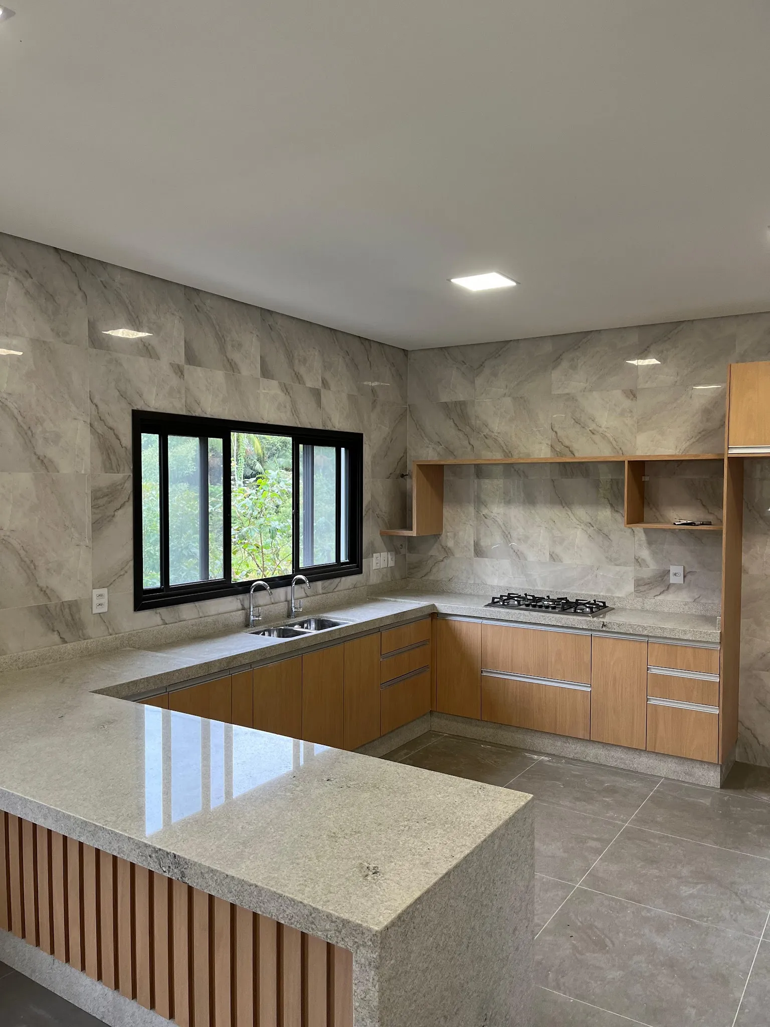 Cozinha em L com bancada de granito claro e armários de madeira